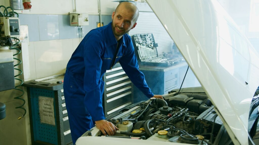 man in blue overall standing beside white car s hood